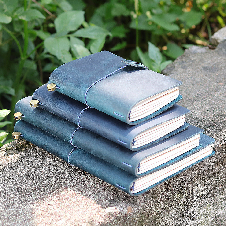 Stack of blue leather journals in several sizes on a stone ledge outdoors