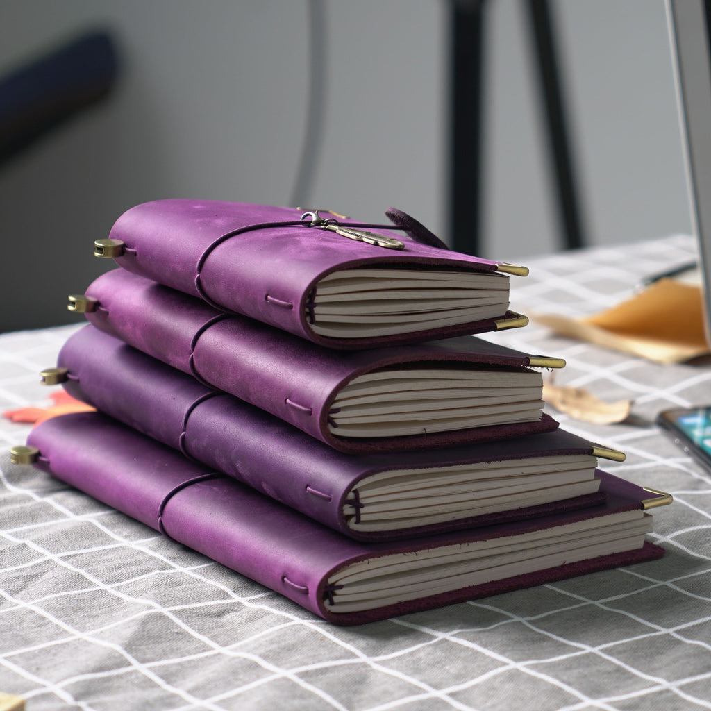 Stack of purple leather journals in several sizes on a checked tablecloth