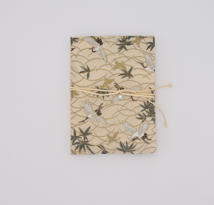 Beige fabric book cover printed with white cranes, green leaves and gold waves, tied with a cream cord