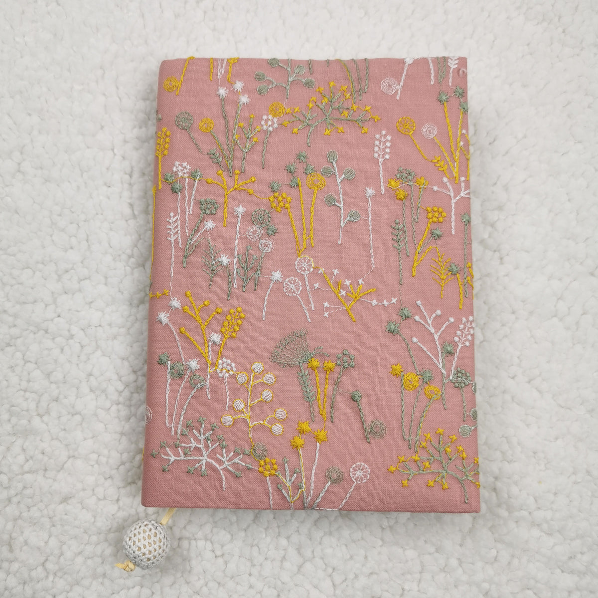 Pink fabric book jacket with embroidery-style yellow, white and sage wildflowers and a cream crocheted bead