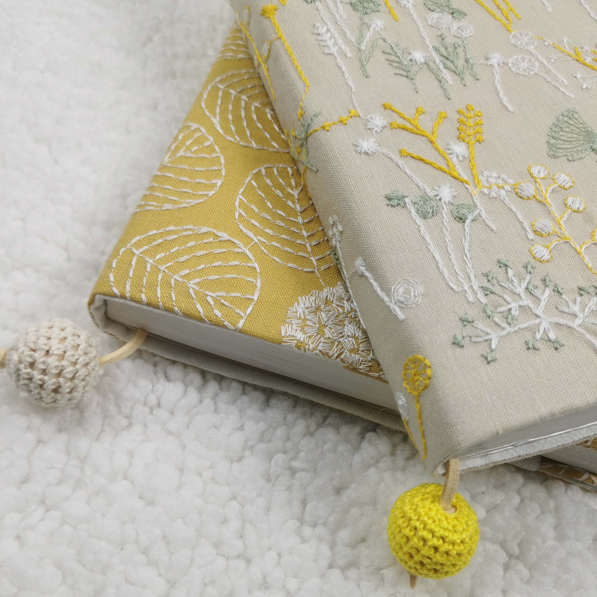 Close view of yellow leaf and beige wildflower fabric book jackets on books, with crocheted beads
