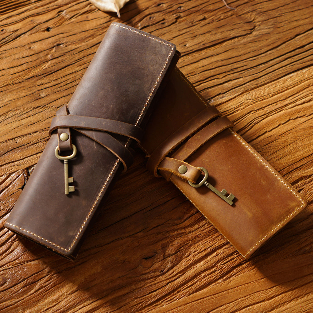 Two leather pen rolls, dark brown and light brown, on a wooden table