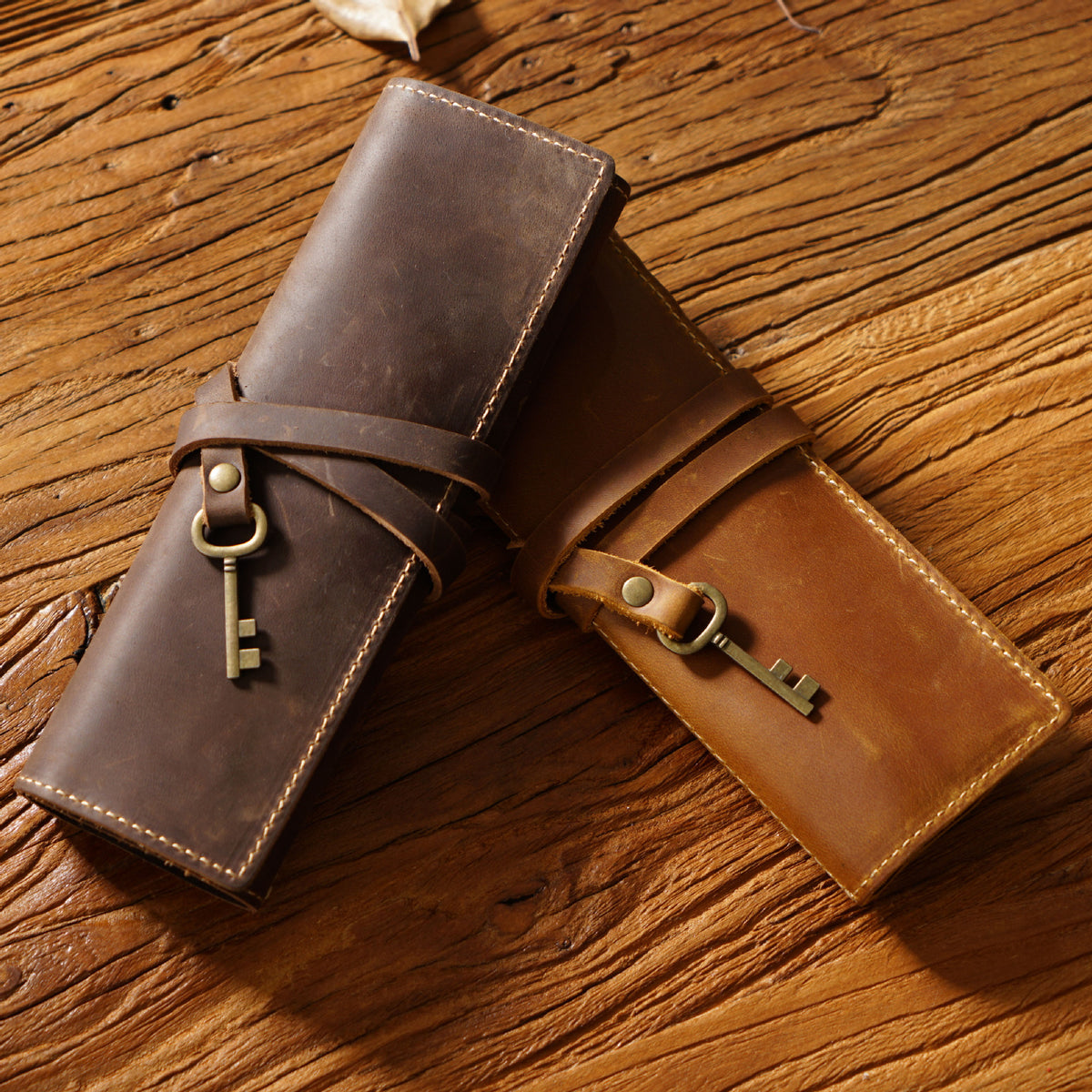 Two leather pen rolls, dark brown and light brown, on a wooden table