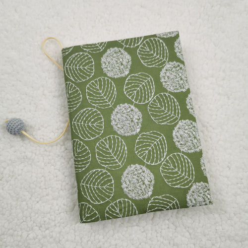 Green fabric book jacket with white embroidery-style leaf outlines and a cord with a grey crocheted bead