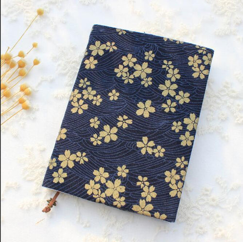 Navy blue fabric book cover with a gold-tone cherry blossom and wave print on a book, with dried flowers