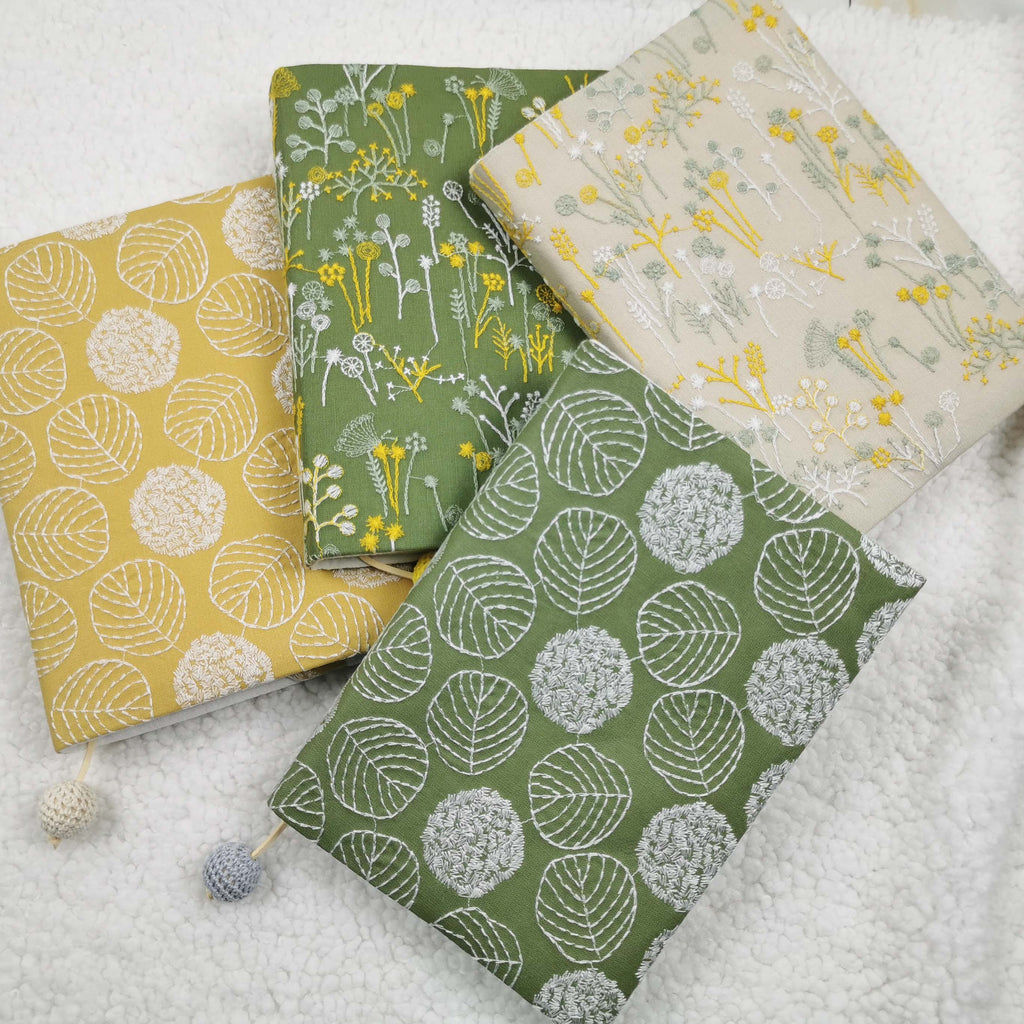 Four embroidery-style fabric book jackets in yellow, green and beige designs with crocheted bead cords
